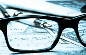 Black eye glasses sitting on top of a newspaper with money and a pen on top.