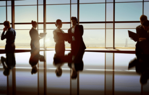 A group of accounting executives meeting around a table with office windows in the background.