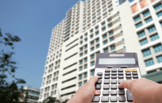 An individual holding a calculator while standing in front of a commercial building in a downtown city.