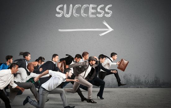 A crowd of professionals in business attire running across a field chasing the word SUCCESS.