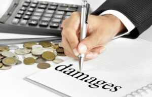 A lawyer writing the word DAMAGES on a steno pad with coins and calculator sitting in the background on table.