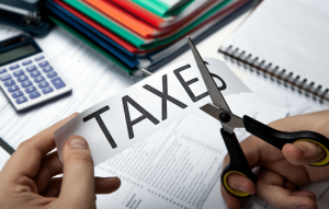 An individual cutting a piece of paper with in half with scissors. The paper has the word TAXES in bold across it.