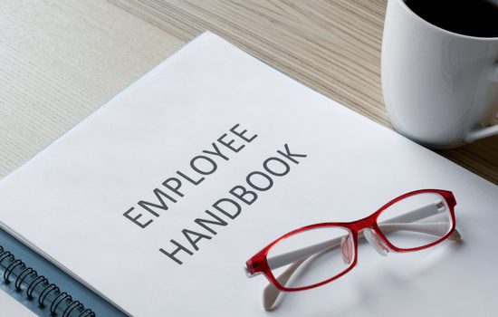 An employee handbook with a pair of red eyes glasses sitting on top with a cup of coffee off to the side.