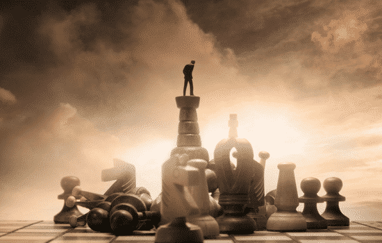 A giant chess board with chess pieces where there is an accountant standing on top of a knight looking around the board.