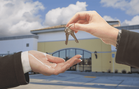 Two individuals standing front of a building, exchanging keys from one to another.