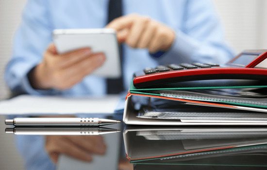 An accountant working on a calculator and a stack of papers and notebooks.