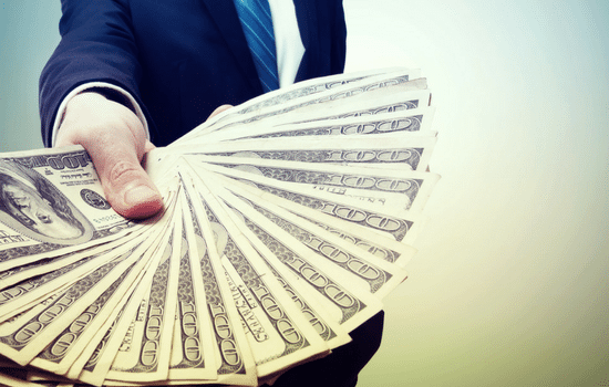 A man in a blue suit holding a fanned out collection of $100 bills.