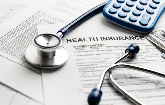 Health insurance forms sitting on a desk. There is a calculator and stethoscope sitting on top of the forms.