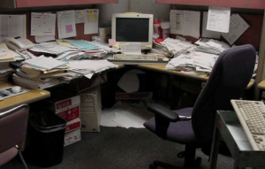 A very messy office cubicle with papers, receipts, forms, and boxes all over the space.