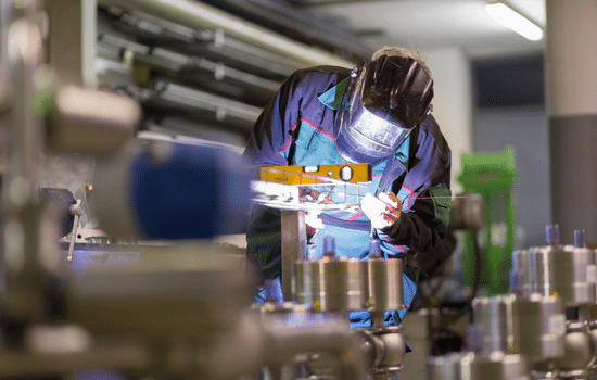 A welder is working on bonding two pipes together at a work station.