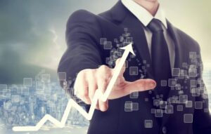 A guy standing in a suit pointing to an arrow showing the rise of digital stock prices.