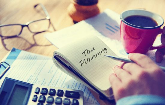 A tax consultant preparing a tax return with a calculator, paperwork and coffee.