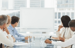 A group of employees meeting in a cityscape office starring at a blank whiteboard.