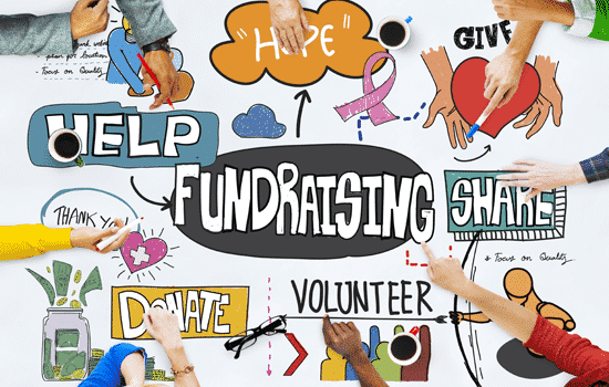 Table with words painted on it, fundraising, help, share, donate, volunteer, give, hope, thank you. People sitting at table pointing to these words.