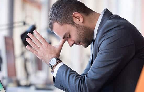 Business Man sits at desk with his head down thinking