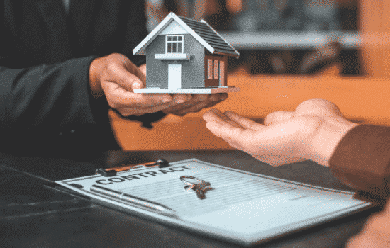 A real estate transaction taking place with someone being given a miniature house momento.