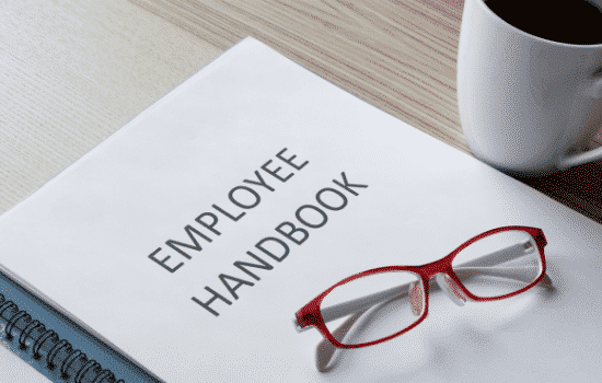 An employee handbook with red eye glasses sitting on top.