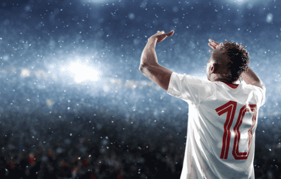 A soccer player celebrating a goal with rain and bright lights shining down on him.