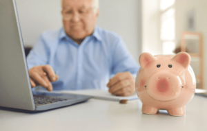 A piggy bank with an elderly man working on a laptop in the background.