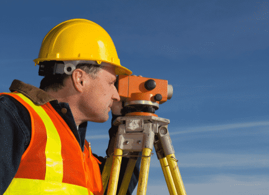 A surveyor looking through his measuring device lens on a construction site.