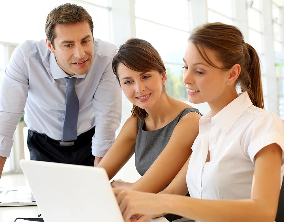 Worker sitting and standing together reviewing a business presentation on a laptop computer.