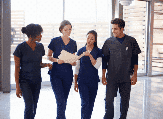 Four nurses reviewing a patient's chart while walking down a hallway.