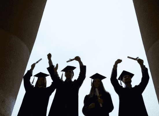 Four graduates celebrating between two columns.