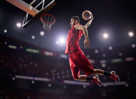 A basketball player is dunking on a goal with stadium lights behind him.