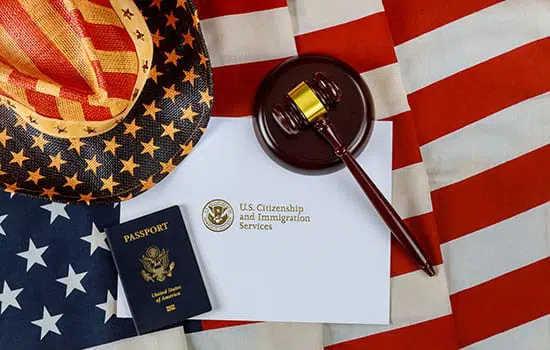 A United States flag with a patriotic hat, gavel, a letter from the US Citizenship and Immigration Services and a passport sitting on top.