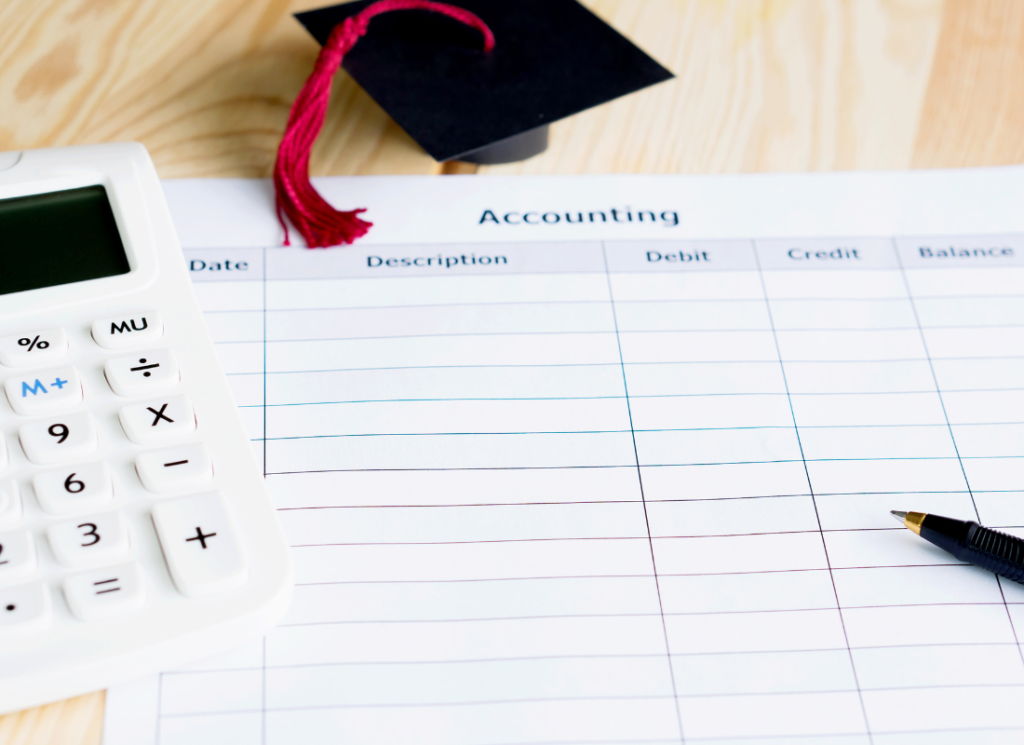 A calculator, pen, and small graduation cap are on top of piece of paper that appears to be a financial statement.