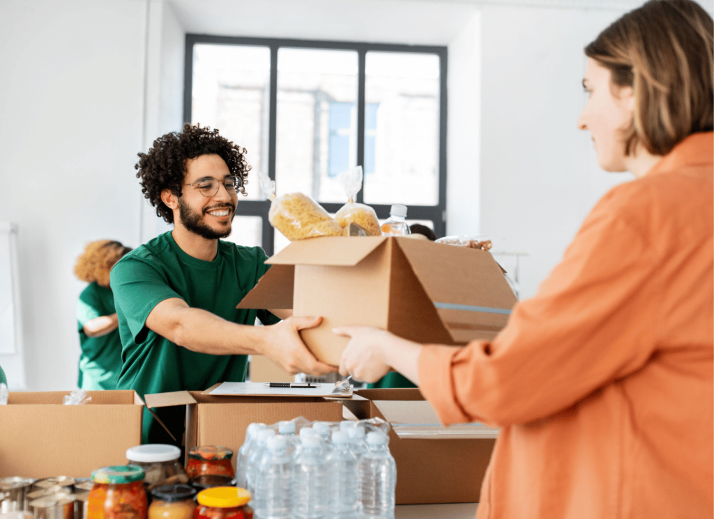 A man receiving donations of food from a woman dress in a orange top.