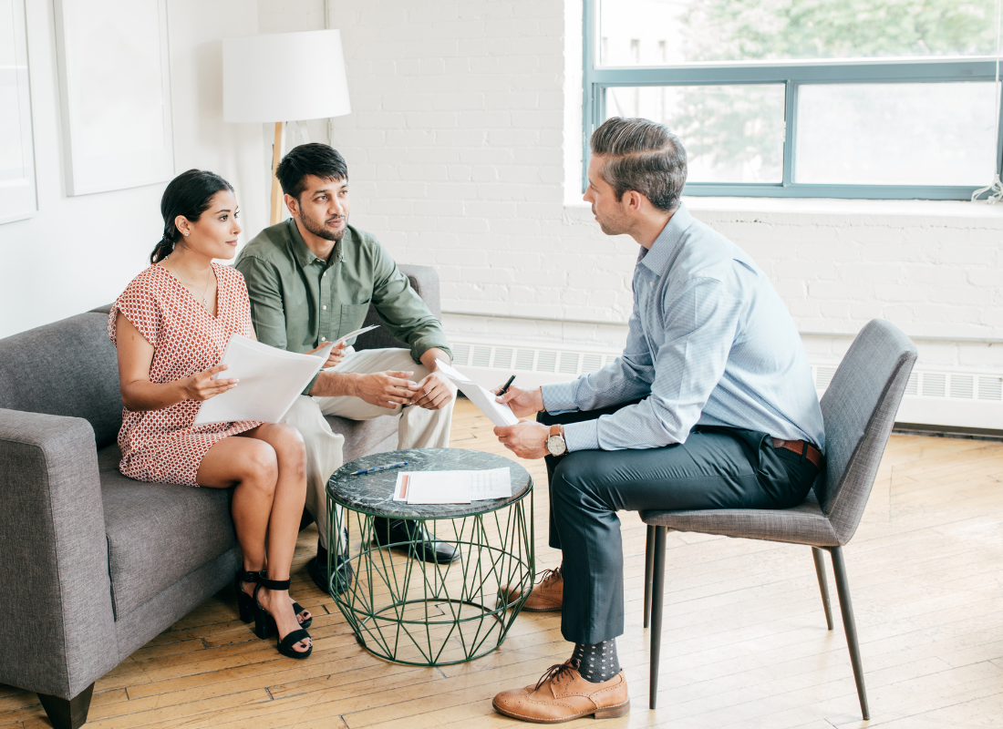 6 Current Benefits Trends_featured img_1100 x 800 A married couple sitting on a couch negotiating a contract with another individual.