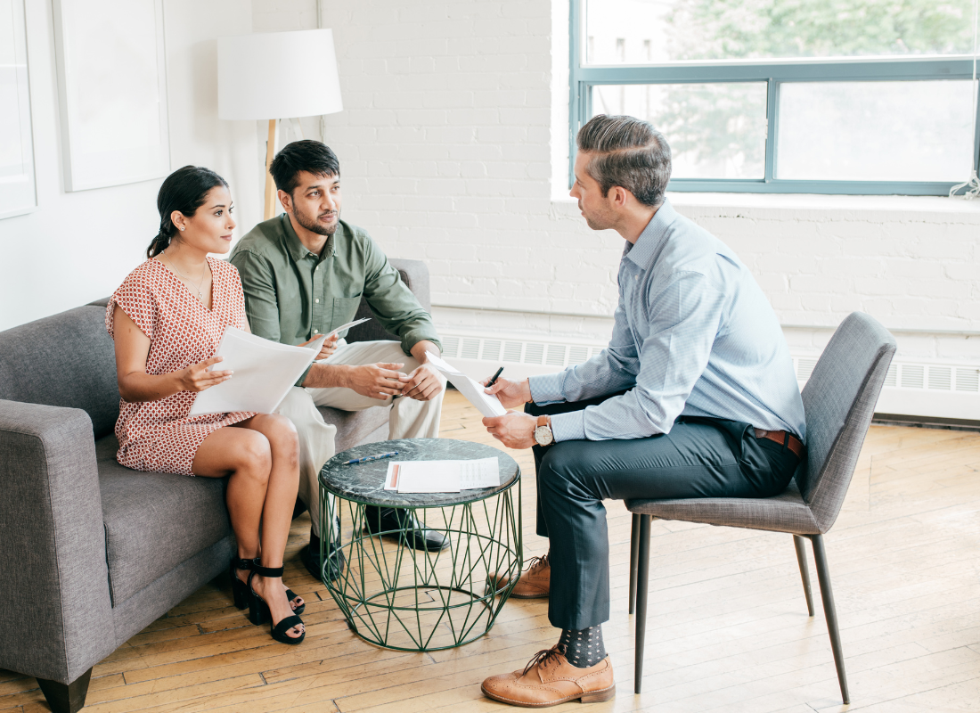 A married couple sitting on a couch negotiating a contract with another individual.