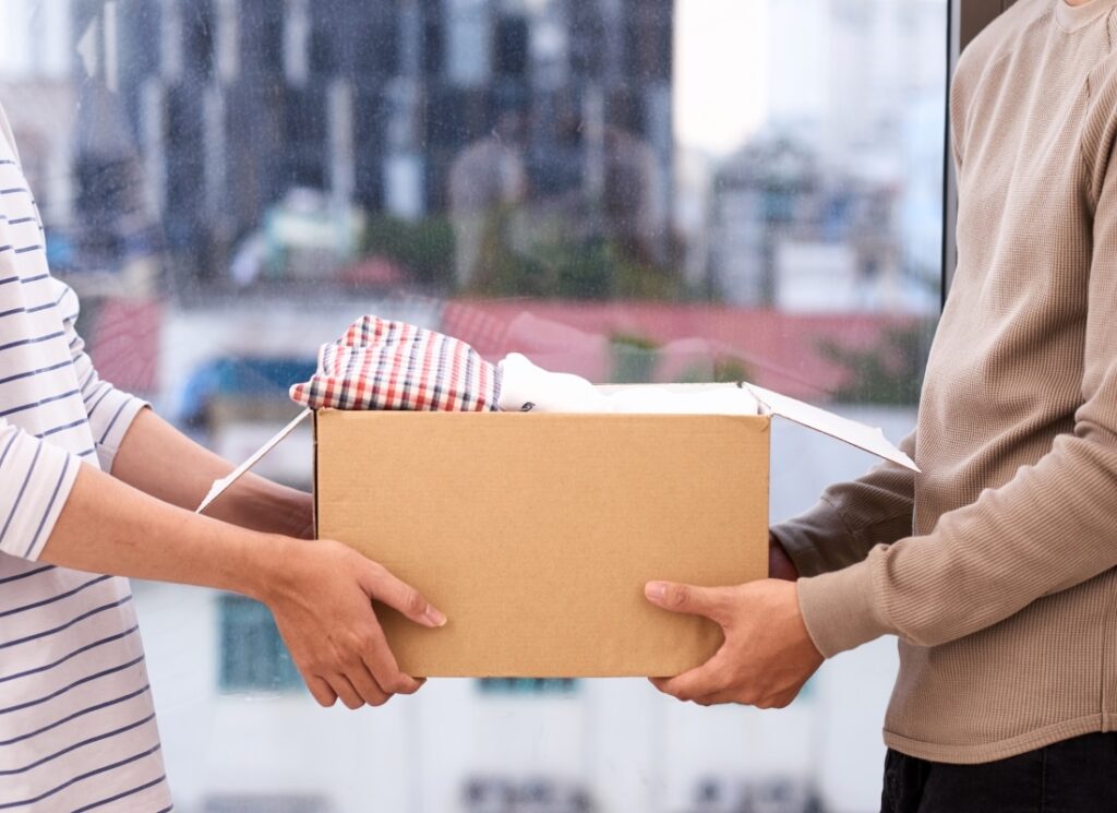 A person is handing a box of clothing to another person.