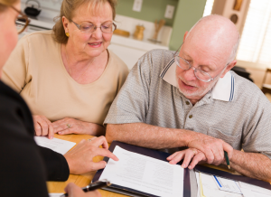 A senior married couple is going over tax papers with their CPA while sitting at a table in their home.