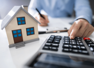 A person is filling out a tax form and typing on calculator. There is a model of a building on the desk.