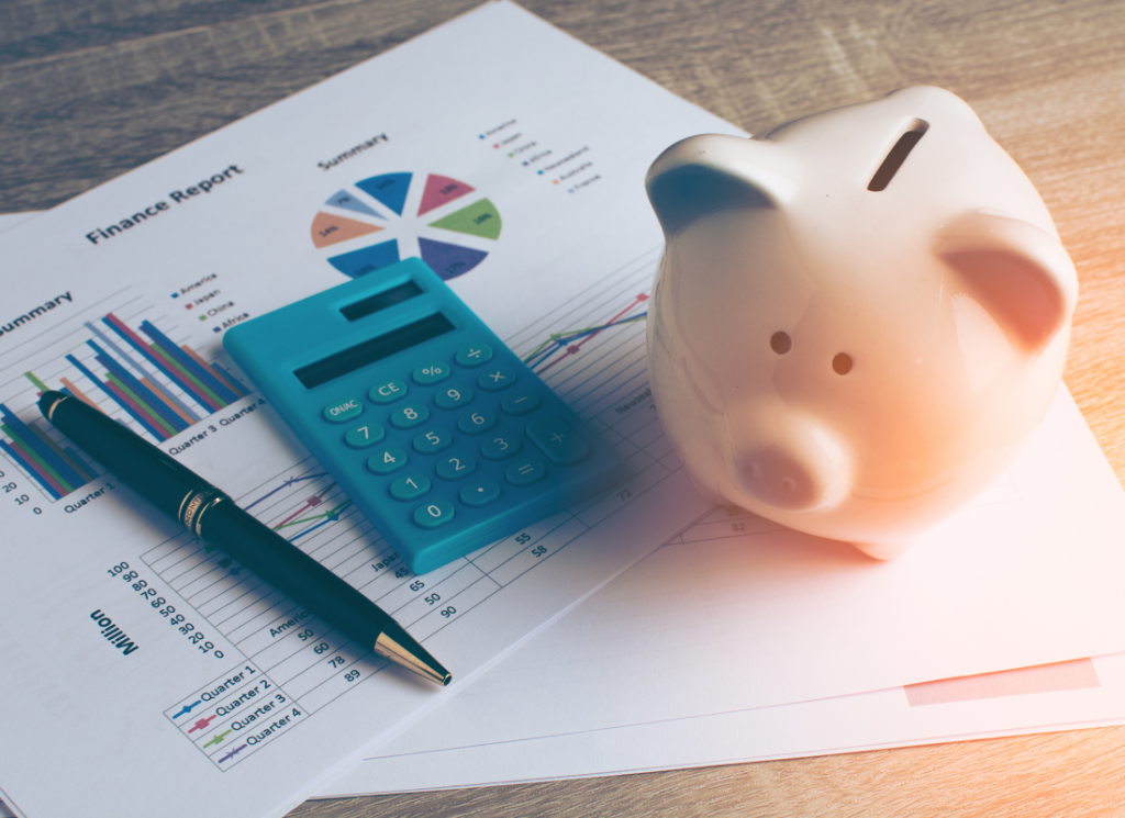 A financial reports is on a desk next to a calculator, a pen, and a piggy bank.