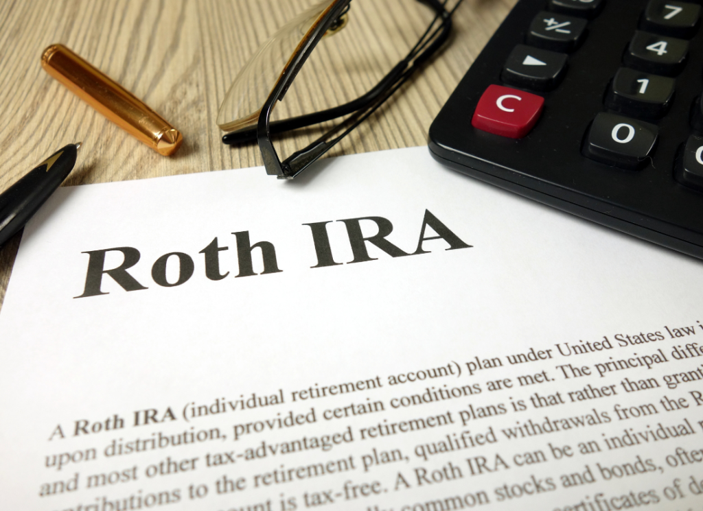 A form with the heading "Roth IRA" is on a table with a calculator, a pen, and a pair of glasses.
