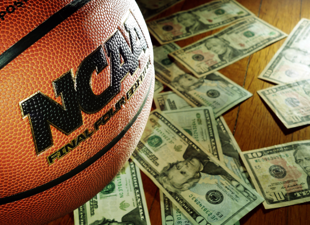 An NCAA basketball is shown on a hardwood floor surrounded by cash.
