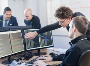 Two AI programmers and IT software developers are working on a desktop computer in an office at a technology company.