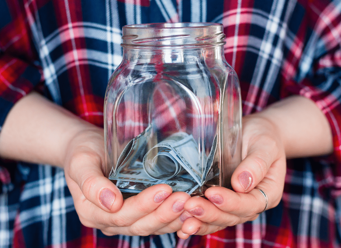 A person is holding a jar with a small amount of cash inside.
