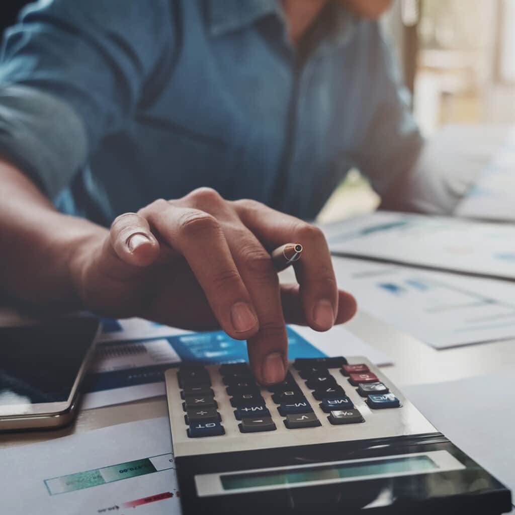 An accountant typing on a calculator with a pen in his hand.