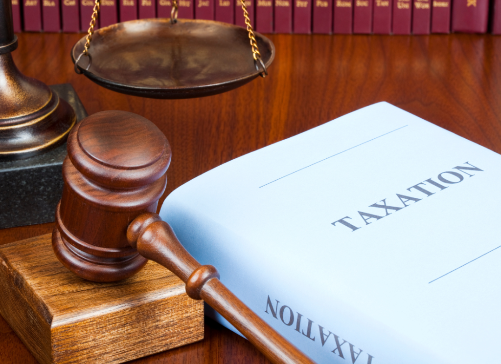 A gavel and balance are on a desk in a law office next to a book with the title "Taxation" written on the front.
