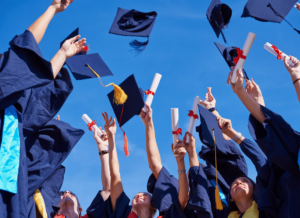 A group of new graduates wearing graduation gowns, are holding up their diplomas and throwing their graduation caps in the air.