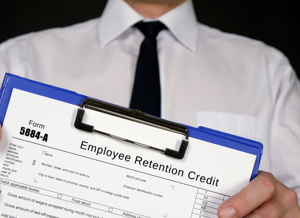 A business person, wearing a white shirt and black tie, is facing forward and displaying a clipboard that holds an Employee Retention Credit form.