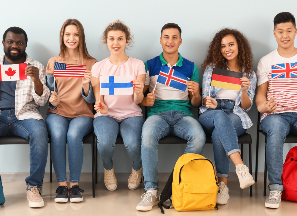 Six students are sitting in a row and holding up a small flag hat represent the country they are from.