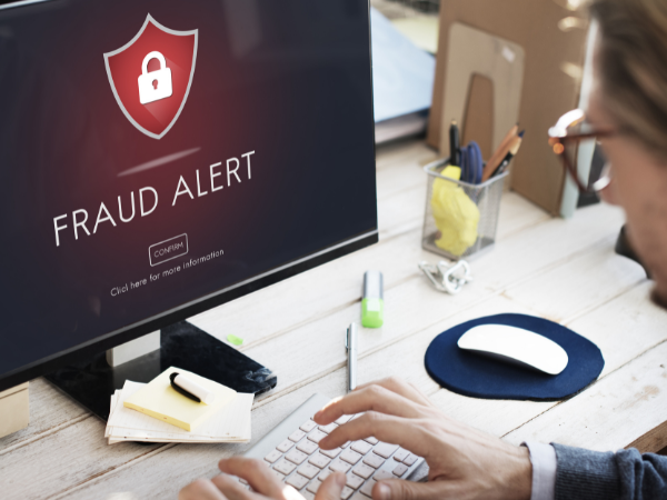 An employee is sitting at a desk with a desktop computer screen showing the words "FRAUD ALERT".