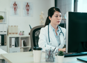 A doctor is working with personal computer and typing in a doctor's office setting.