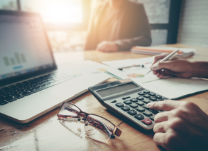 Businessman and partner are sitting at an office desk using a calculator and laptop for calculating finances and tax credits.