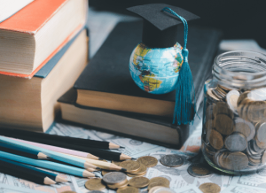 A globe and a jar filled with foreign coins sit on a desk in a classroom. There are books, pencils, and cash on the desk as well.